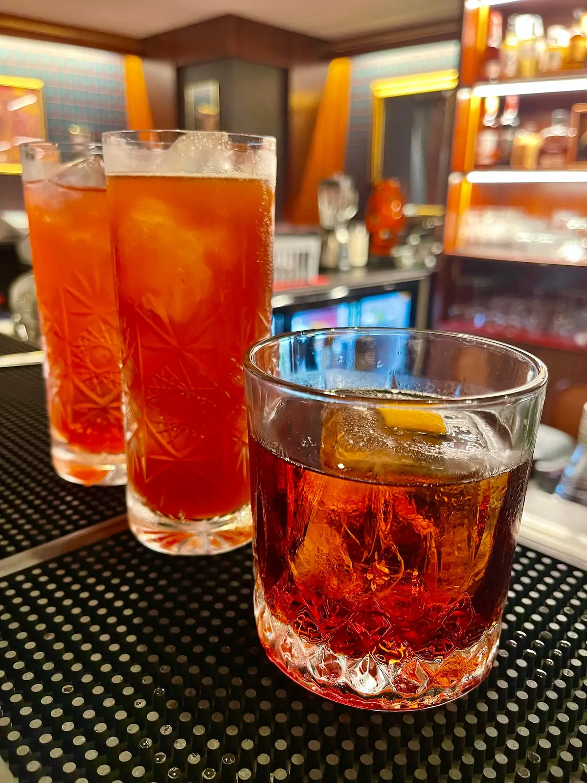 Negroni e due long drink nel cristallo molato appoggiati sul tappetino del bancone