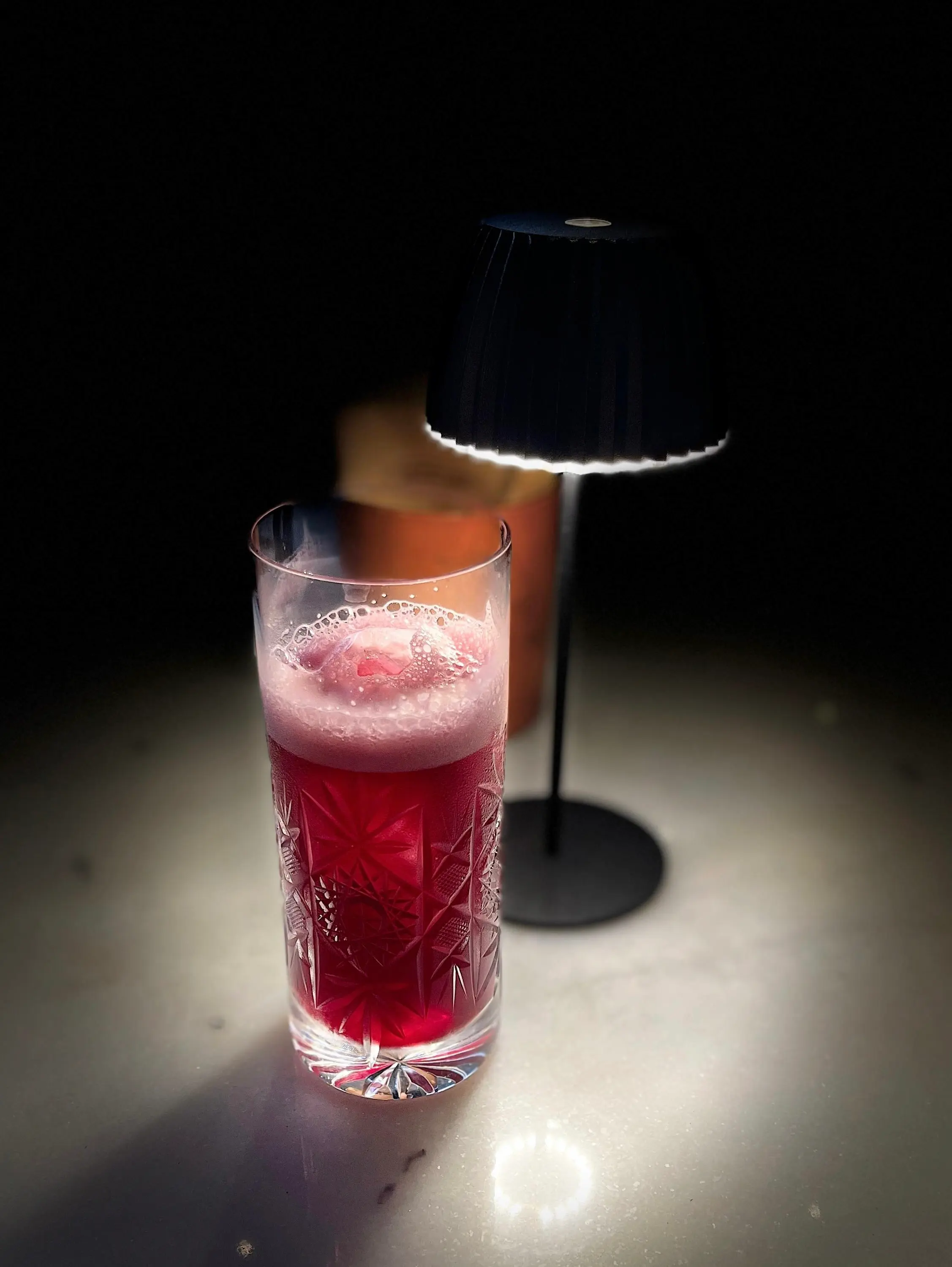 Signature drink rosso in bicchiere di cristallo molato illuminato da una lampada da tavolo