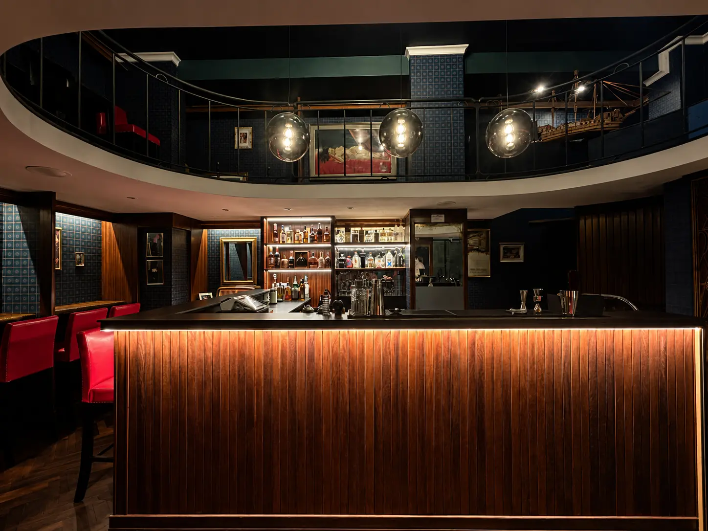 Il bancone in mogano retroilluminato del cocktail bar Gentleman a Lecce, con il soppalco e le lampade a globo